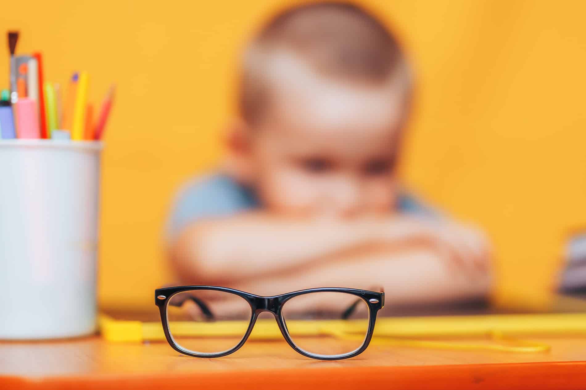 Boy sitting at his desk with a glasses infront of him after learning about early signs for vision problems in kids